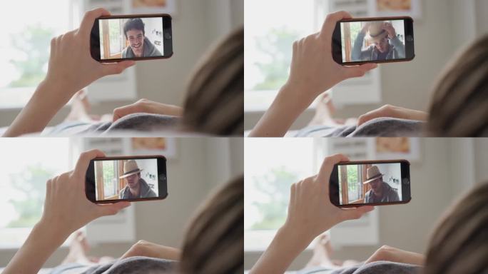 年轻女子拿着智能手机摄像头和躺在家里床上的朋友进行视频聊天