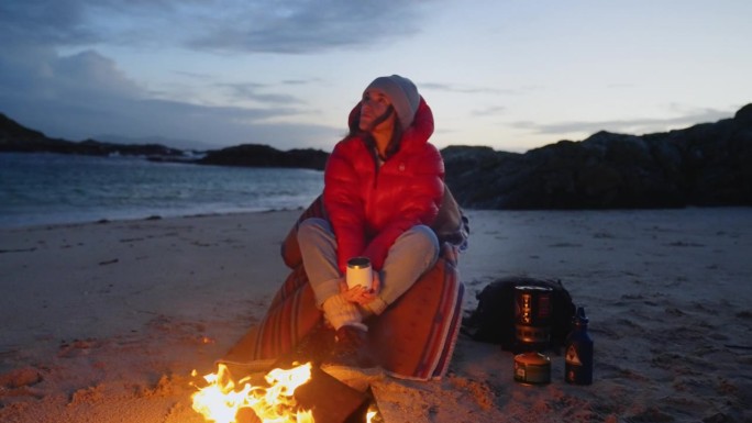 在寒冷的天气里穿着保暖衣服露营的妇女。在沙滩上用营火热身