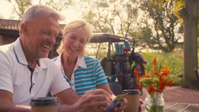 老夫妇在打完一轮高尔夫球后坐在一起喝咖啡，看着记分卡