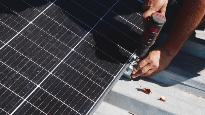 工人在金属支架上安装太阳能电池板(特写)。房屋屋顶人工安装光伏太阳能板的近景。工程师在户外工作。
