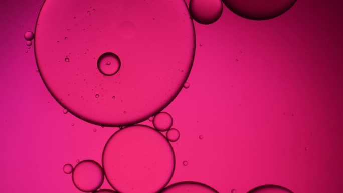 粉红色的油珠飘浮在水面上。粉彩泡沫的背景。橙色背景的油滴。