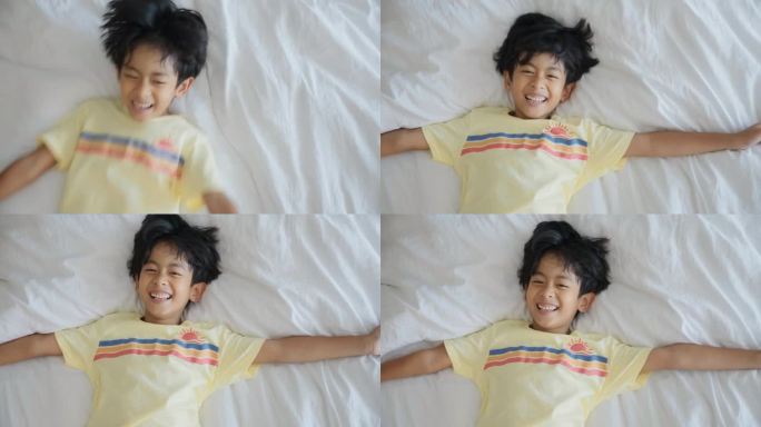 可爱活泼的小男孩跳下来，躺在舒适柔软的床上，双臂举起，微笑着感到快乐。