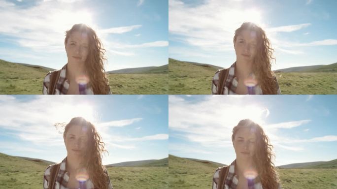美丽的年轻女子在大自然中微笑，头发随风飘扬的特写肖像徒步旅行者女孩站在太阳耀光前在苏格兰慢动作徒步旅