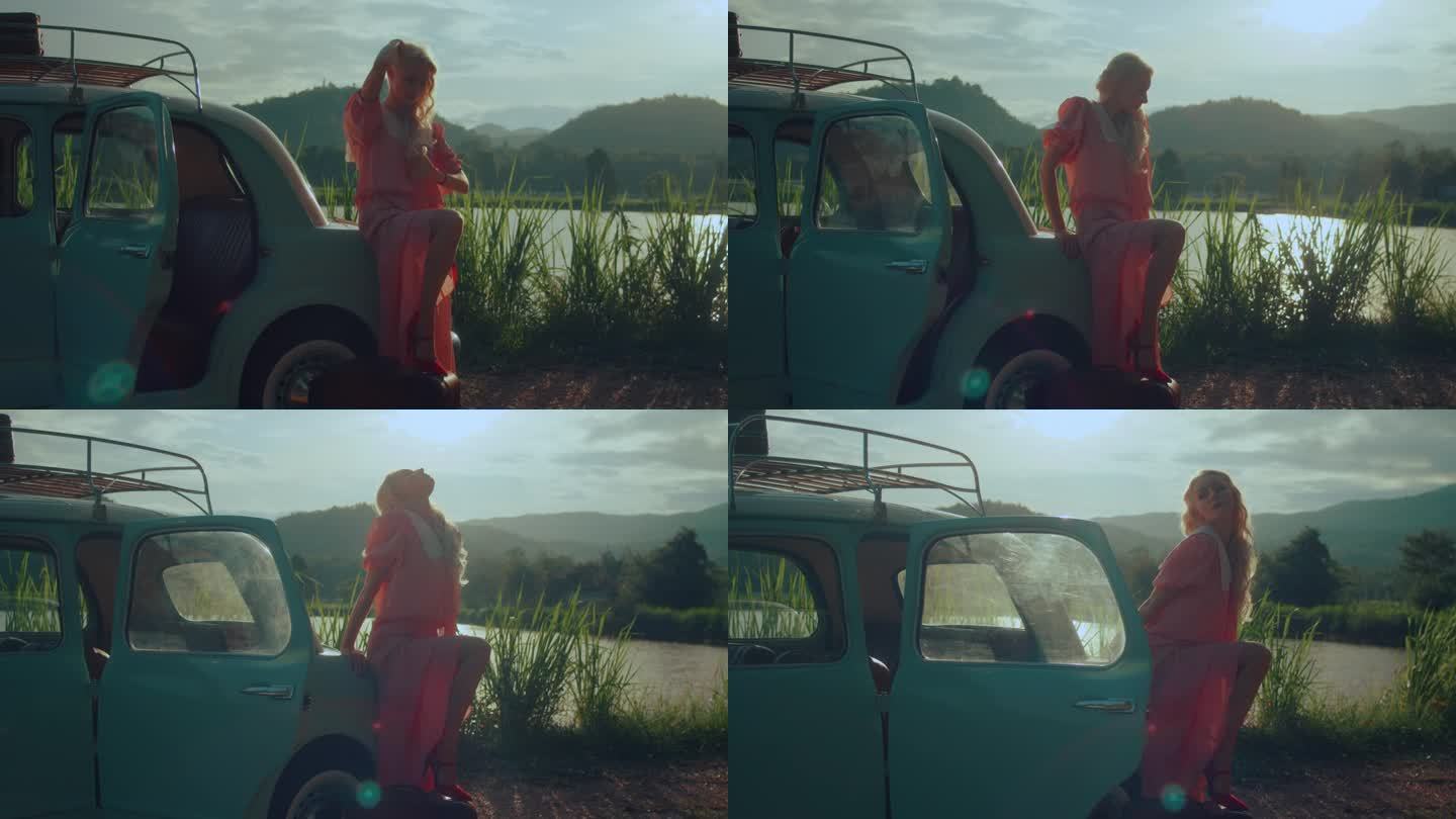 一个穿着粉色复古裙的女孩坐在一辆蓝绿色复古车的后备箱上