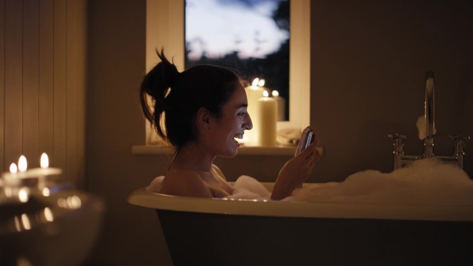 美女躺在泡泡浴里，用智能手机摄像头和家里的朋友视频聊天