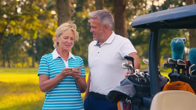 一对老年夫妇站在高尔夫球场的马车旁，一起在记分卡上打分