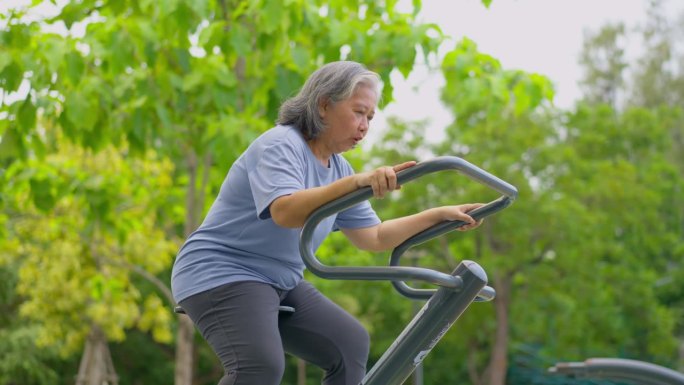 在公园健身站随意锻炼的亚洲老年妇女。代表以运动永葆青春，露天健身，身体健康的理念。城市公园户外健身器