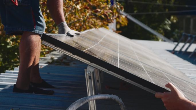工人在金属支架上安装太阳能电池板(特写)。房屋屋顶人工安装光伏太阳能板的近景。工程师在户外工作。