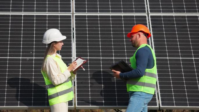 一男一女投资者戴着头盔，穿着特殊的制服，站在太阳能电池板的背景下。广告理念为成功的商业、生态和金融