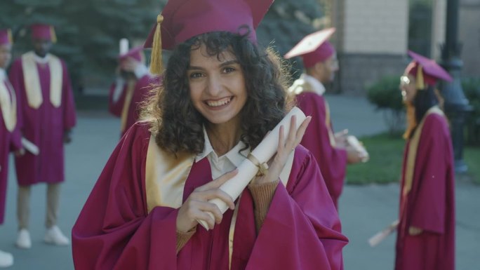 在大学附近的户外，戴着毕业帽、穿着毕业袍、拿着毕业证书的兴奋的年轻女士的肖像，表达着幸福