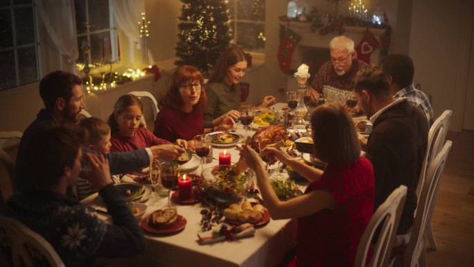 不同群体的人，年轻人和老年人，分享一个快乐的圣诞晚餐在家里。一家人坐在摆满美味烤火鸡大餐的大餐桌后面