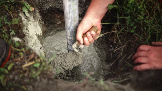 工人用混凝土铲将混合物撒在挖入地下的钢管周围