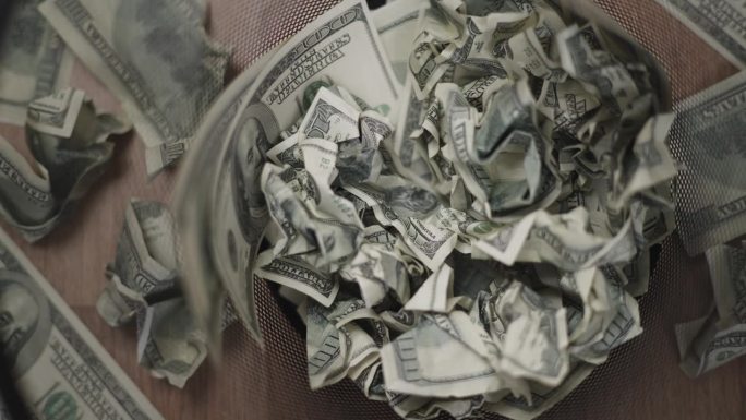 镜头小车拍摄，俯视图的许多美元钞票被揉成一团，扔进废纸篓和木地板，商业金融概念。