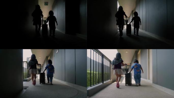 一个亚洲小女孩和她的弟弟走在酒店的走廊上，手里拿着旅行行李。