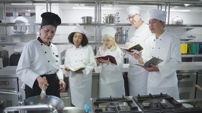 多种族厨师学生在烹饪课上学习炒菜准备课程，包括翻锅技巧和笔记，高级厨师讲师讲授食物准备课程
