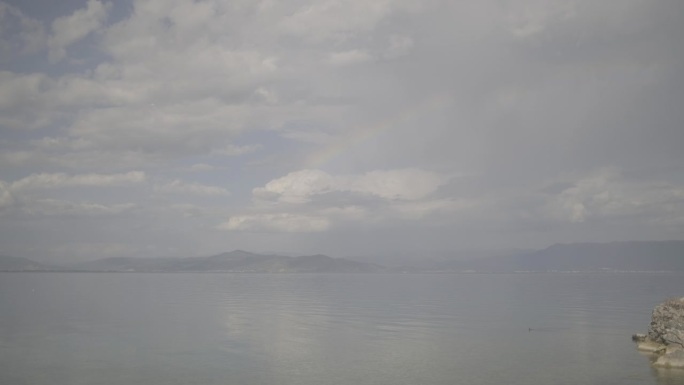 在一个多云的日子里，从阿尔巴尼亚林拍摄的镜头显示马其顿在背景中，在云和蓝色的水周围形成了美丽的彩虹