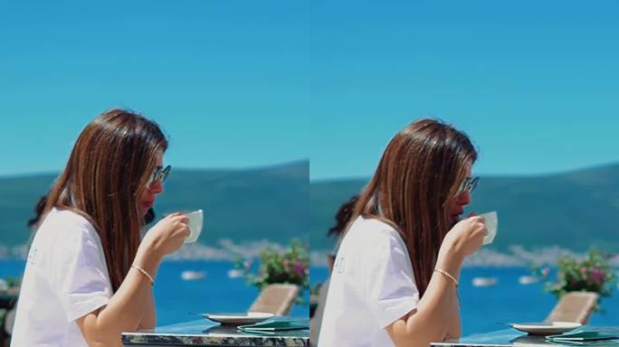 年轻的女孩微笑着坐在海边餐厅的咖啡馆里喝咖啡