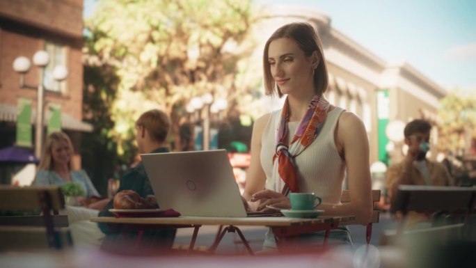 女自由职业者使用笔记本电脑在咖啡馆远程在线工作。在一个阳光明媚的夏日，在露台上远程办公时，年轻的创意