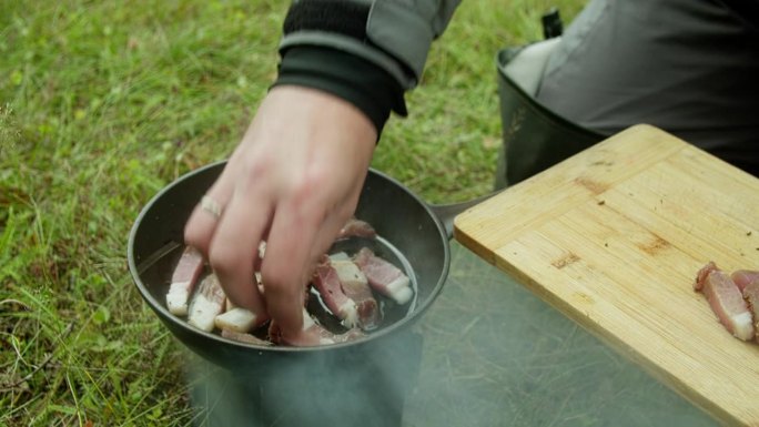 一个男人把肉和猪油放在煎锅里煎。