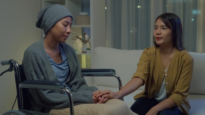 年轻的亚洲人牵手信任安慰帮助癌症患者说话哭泣晚上在家里的客厅减压。医疗保健。