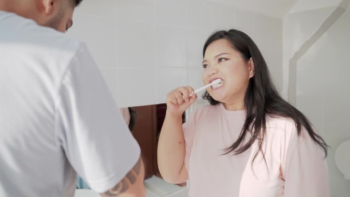 亚洲中年夫妇拿着牙刷在浴室里一起刷牙。快乐的可爱的中年夫妇刷牙，用修复和保护牙膏修复牙齿的敏感区域的