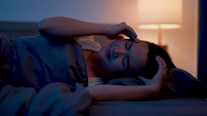 一个亚洲女人晚上躺在床上头痛。
