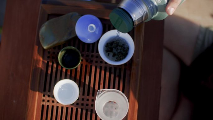茶艺师在木桌上将保温瓶里的水倒入碗中泡茶。
