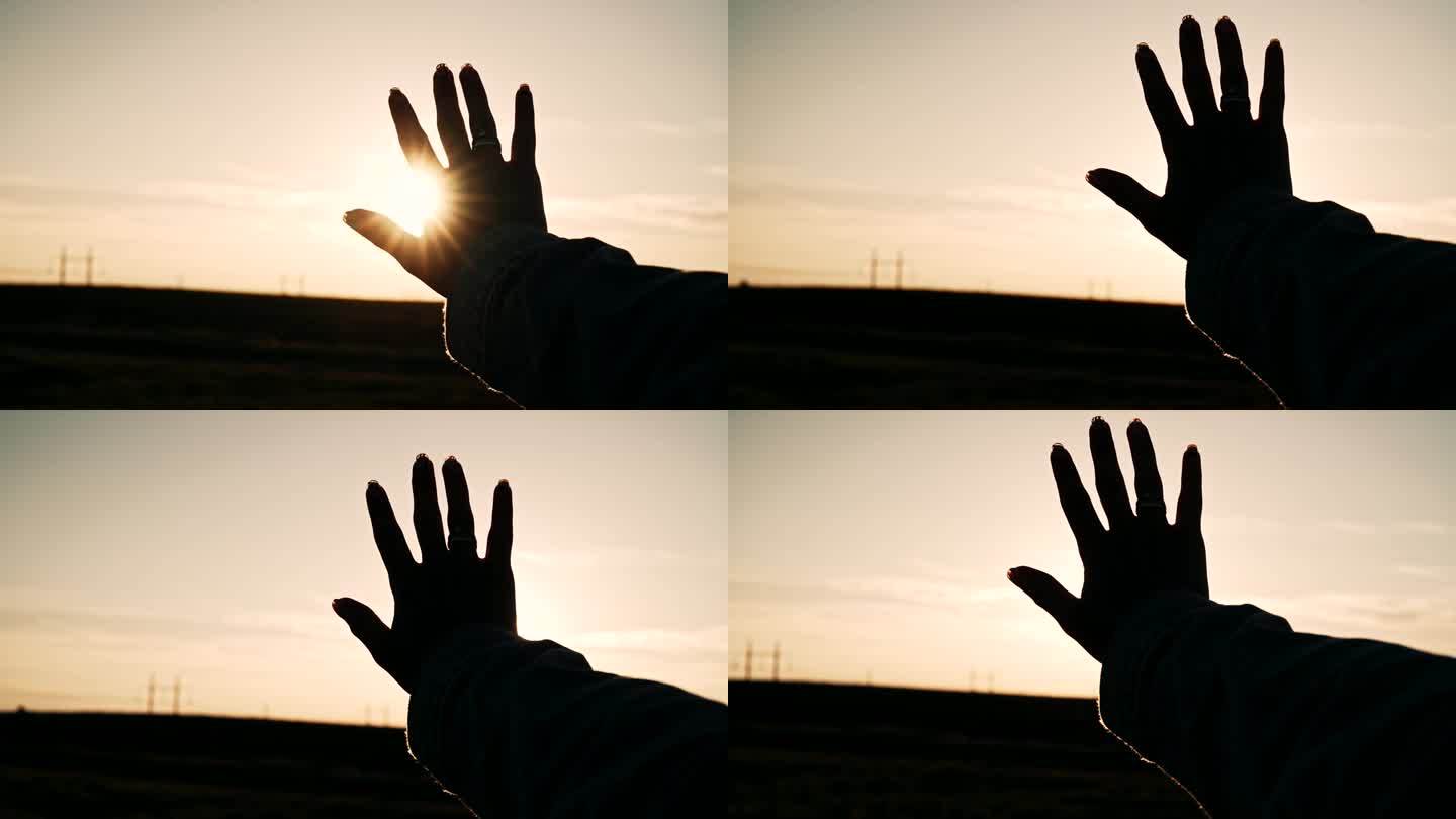 女性的剪影抚摸温暖的光线，夕阳时分。女人的手掌。阳光穿过指缝。与自然团结，爱，信仰和希望的标志，善良