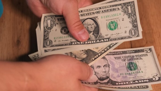 男性用手数着面值为1美元、5美元、20美元和100美元的钞票;