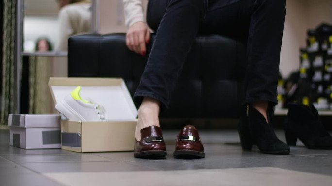 一个无法辨认的白人女人的腿坐在店内试穿新鞋。自信时尚的购物者在黑色星期五的商店里挑选鞋子。