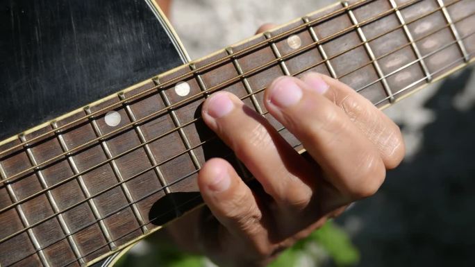 一个人在户外弹吉他。弹原声吉他的人。在阳光下练习吉他的人。播放音乐。拨动原声吉他。播放原声音乐