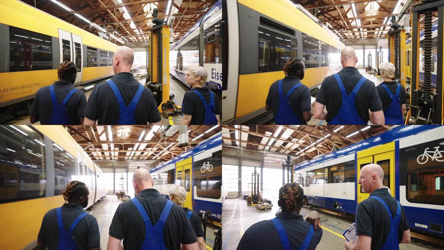 三名火车工程师走过列车，在维修车间讨论任务的后视图