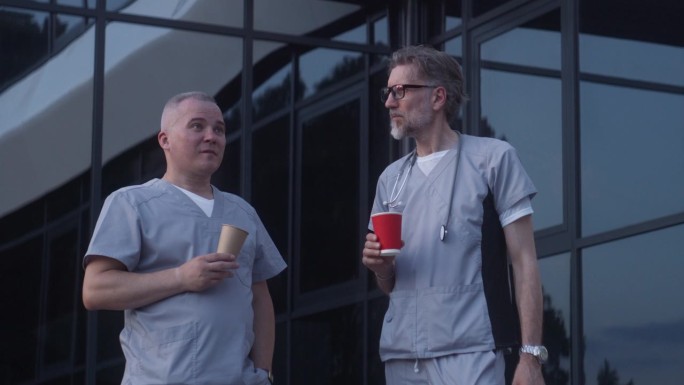 两位医生站在医疗中心入口附近，喝着咖啡，讨论着工作