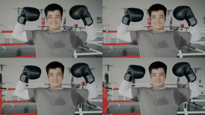 快乐的亚洲拳王站在拳击场上，举起双臂，微笑着看着镜头