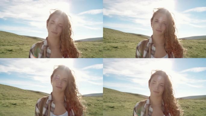 美丽的年轻女子在大自然中微笑，头发随风飘扬的特写肖像徒步旅行者女孩站在太阳耀光前在苏格兰慢动作徒步旅