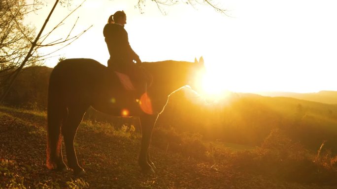 一个女人骑在马上看着日出越过丘陵的乡村