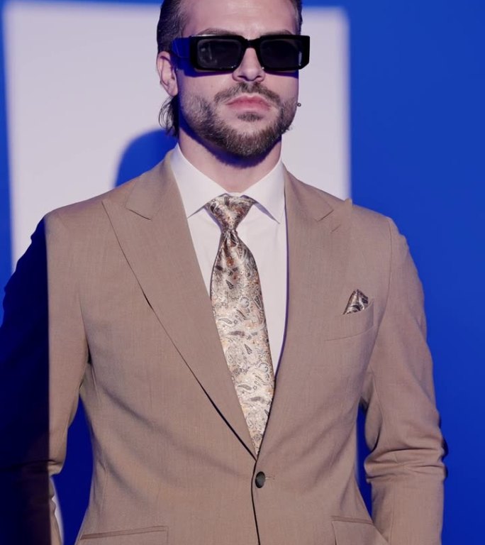 垂直视频酷时尚男子与太阳镜的手在口袋里，在灰色的背景前向前看