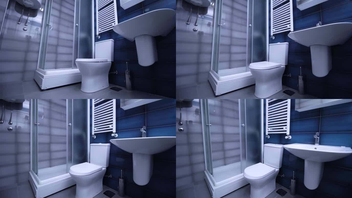 现代公寓里的浴室。崭新干净的马桶，贴着蓝灰瓷砖。垂直摄像机移动。