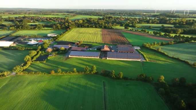 现代农业的航拍画面:谷仓屋顶上安装了光伏板的畜牧场，农田和草地上的沼气厂沐浴在阳光的柔和拥抱中。