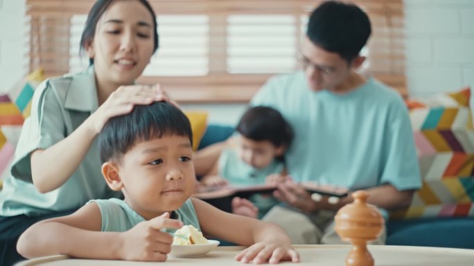 一个小男孩正在家里吃蛋糕，而他的父母和妹妹正在弹吉他