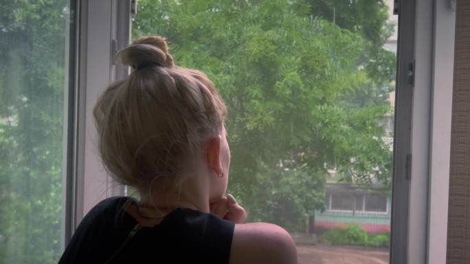 一个悲伤的女孩在下雨和恶劣的天气里望着窗外。
