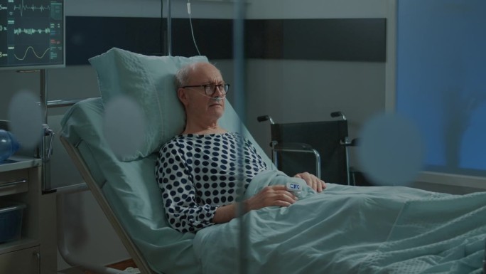 生病的老人带着血氧计躺在医院的病床上