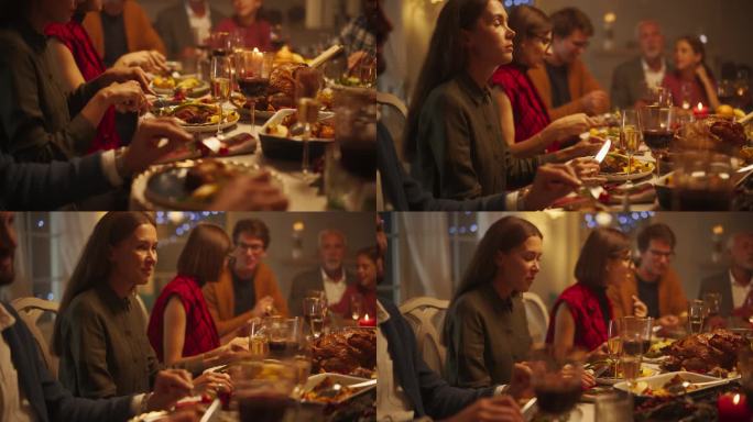 一个美丽的女性享受节日大餐的肖像，与家人和朋友坐在餐桌后面，享用美味的火鸡大餐。客人在家里有有趣的谈