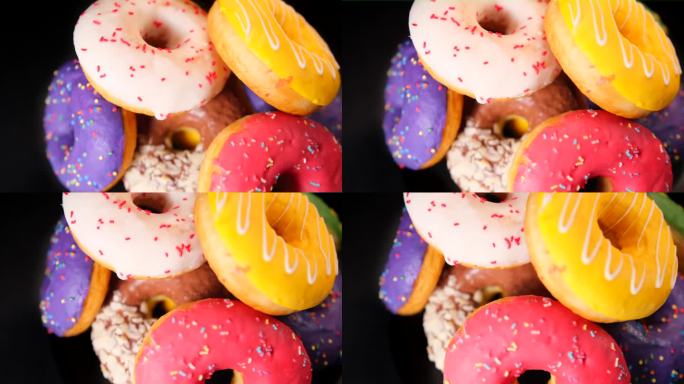 旋转特写镜头山的彩色甜甜圈与各种奶油软糖，孤立的黑色背景。
