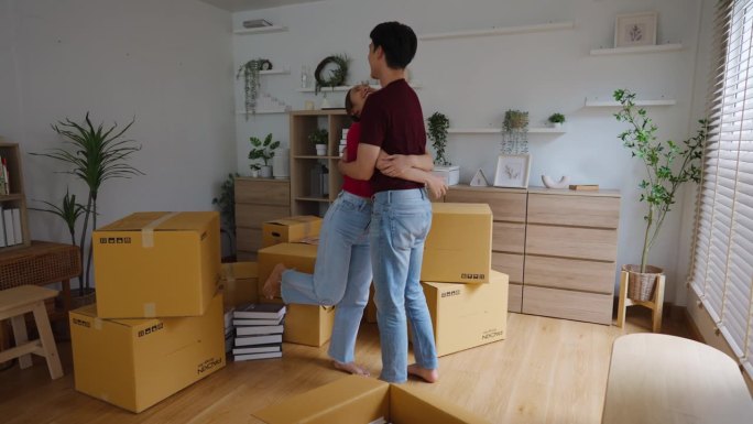 一个年轻的女人抱着她的男朋友开心地买了她自己的房子，在旧房子里堆满了纸箱。为男女夫妇组建家庭