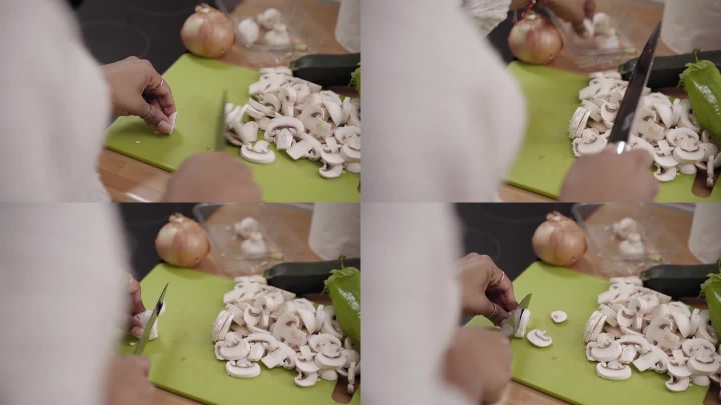 无法辨认的年轻黑人女孩在家里用刀在绿色塑料板上切鲜蘑菇。
