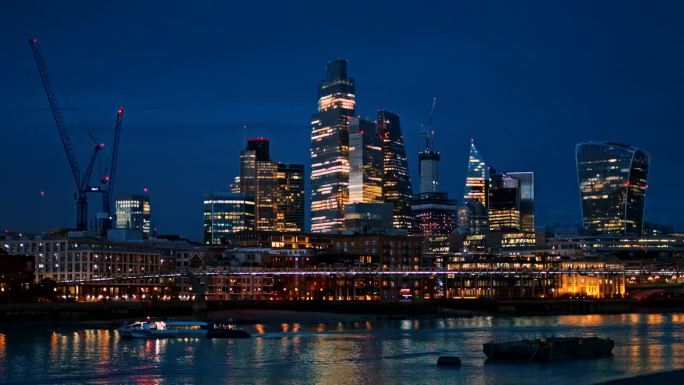 伦敦市中心的夜景，英国。市区的摩天大楼，泰晤士河上的千年桥和漂浮的船，大量的照明