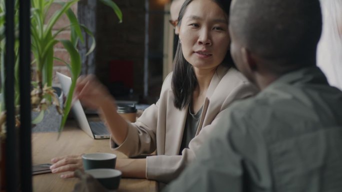亚洲女商人在共用办公空间用智能手机和非裔美国男同事聊天