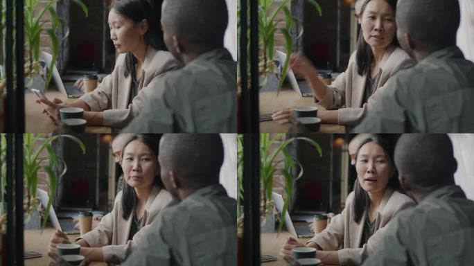 亚洲女商人在共用办公空间用智能手机和非裔美国男同事聊天