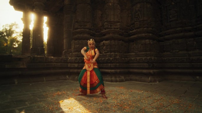 穿着传统服装的印度妇女看着镜头，穿着五颜六色的纱丽跳舞的慢动作肖像。富有表现力的年轻女性在庙里表演民